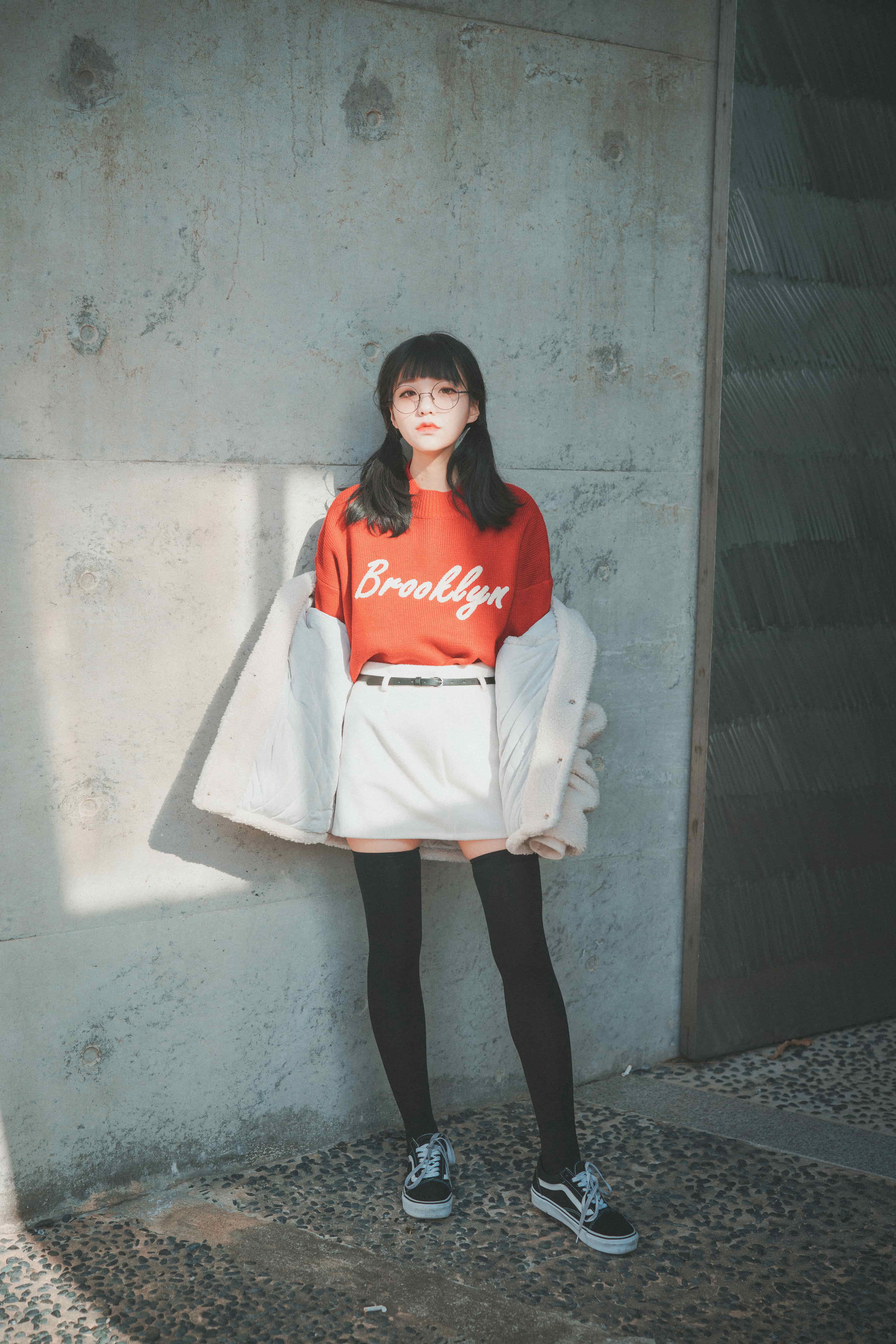 Close framing of stocking-clad legs against brick, one foot bare and planted, showing nylon texture and gentle arches.